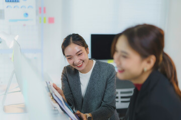 Two young businesswomen are enjoying a moment of laughter together while working on a project in their modern office