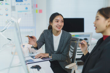 Two businesswomen are discussing work, smiling and pointing at documents with pens