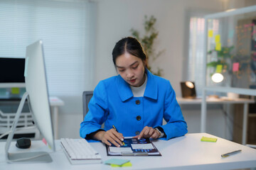 Young asian businesswoman is analyzing charts on a clipboard while working at her desk in a modern office