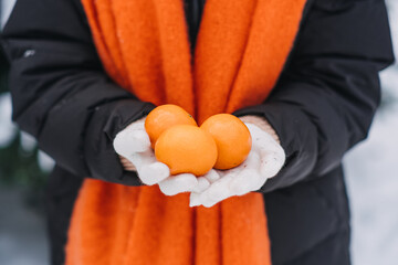 Close-up of woman holding an orange in a snowy outdoor scene. Winter immunity, fresh citrus, healthy living during cold season