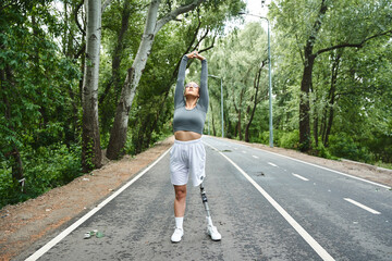 A determined young woman stretches outdoors, embracing fitness and nature with her prosthetic leg.