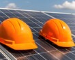 © Rossarin - Two bright orange safety helmets are placed on solar panels under a clear sky, symbolizing construction and renewable energy work.