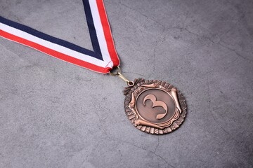 Bronze medal with striped ribbon on grey background, closeup