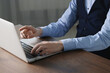 © New Africa - Businessman using laptop at wooden table indoors, closeup. Modern technology