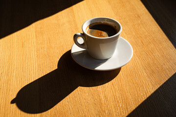 A cup of black coffee on the table in the sunlight