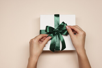 Woman decorating gift box with bow on beige background, top view