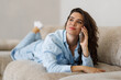 © F8  \ Suport Ukraine - Relaxed young woman lies on a sofa, talking on a smartphone in a cozy, modern living room.