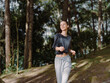 © SHOTPRIME STUDIO - Smiling young woman jogging in the forest, wearing comfortable athletic attire Nature and fitness concept, with green trees and sunlight filtering through branches