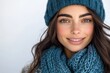 © netrun78 - A cheerful brunette woman smiling brightly in a vibrant navy winter hat and scarf against a solid white background, radiating warmth and happiness