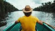 ©  Shomixer - A man in a bright yellow shirt rows a wooden boat through a wide, serene river, surrounded by expansive greenery, symbolizing adventure and solitude.