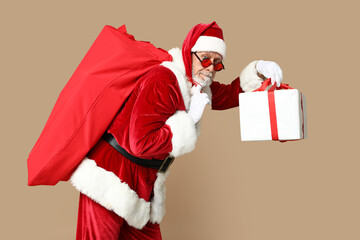 Poster - Santa Claus in sunglasses with bag full of gift boxes on brown background