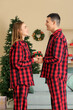 © Pixel-Shot - Young couple in plaid pajamas giving gifts in living room decorated for Christmas