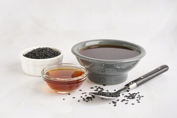 Bowls of oil and sesame seeds with spoon on white background