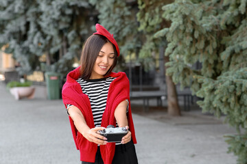 Poster - Beautiful young happy Asian woman in stylish red beret with camera on city street