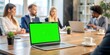 © Visual Vibes - Laptop display with green screen background on an office desk while people attend a business meeting. Isolated mockup template with blank chroma key and free space on computer monitor. Closeup.