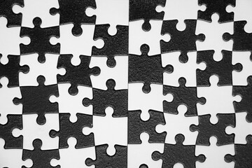 A jigsaw puzzle with black and white pieces. The puzzle is made up of many small alternating pieces from black and white. Concept of challenge and accomplishment by working together.