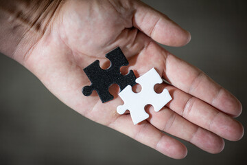 A hand holding two puzzle pieces, one white and one black both pieces have the same shape. The choice is a difficult concept.