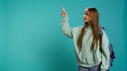 Radiant woman pointing finger towards empty space doing advertising, talking with audience. Smiling young girl doing presentation, showing copy text, studio backdrop, camera B