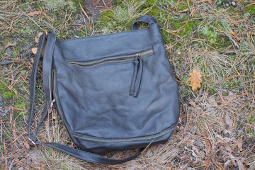 one black old leather bag lies on the grass and ground in nature