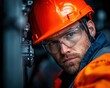 © Rossarin - A focused worker in an orange hard hat and protective gear examines machinery with determination.