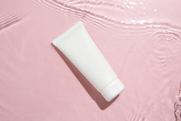 Poster - Cosmetic product. Tube with cream in water on pink background, top view