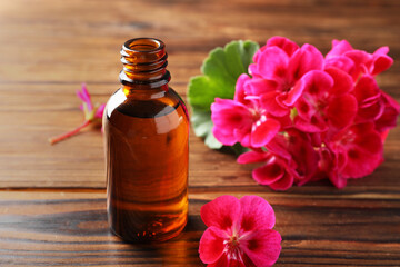 Poster - Geranium essential oil in bottle and beautiful flowers on wooden table