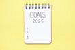 © TATIANA - The inscription goals 2025 on notepad on yellow background, top view.