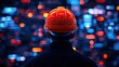 © Vodkaz - Worker in an orange hard hat, observing digital data visualization at night.