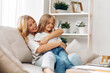 © SHOTPRIME STUDIO - Mother and daughter sharing a heartfelt moment on the couch, embracing each other with smiles and warmth