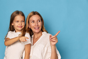 Mother and daughter happily pointing at something in a portrait photo against a blue background