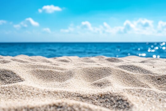 Closeup of soft white sand on a beach with a blue ocean and sky in the background.