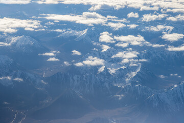 Mountains view from above. Kamchatka Peninsula, Kamchatka Krai, Russia. Beautiful aerial photo of mountainous terrain. Clouds over snow-capped mountain peaks. Air travel to the Russian Far East.