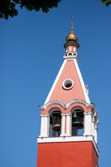 A red and white tower with a gold dome and a bell