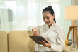 © Prathankarnpap - Attractive young entrepreneur using digital tablet on sofa at home