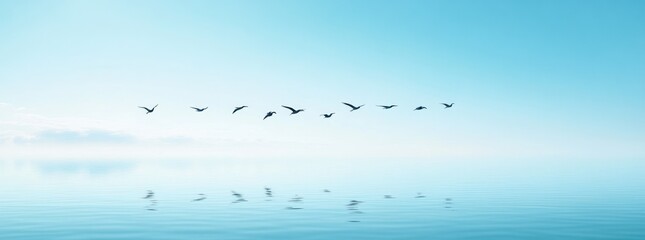 A flock of birds flies in formation over a calm body of water with a blue sky and white clouds in the background.