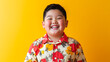 © Pangsiri - Brightly smiling chubby Asian boy in colorful floral shirt against vibrant yellow background, radiating joy and happiness