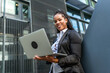 © unai - Modern latin businesswoman working using laptop outside a financial building