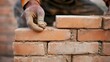 © aubriella - A close-up of a bricklayer carefully placing bricks, looking at the camera with concentration, Bricklaying site scene
