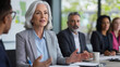 © Denis Yevtekhov - Older woman confidently leading a board meeting in a modern conference room, colleagues listening attentively, professional attire, leadership, diversity, STEM environment