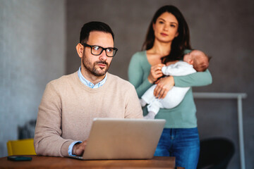 Wall Mural - Father businessman try to work on laptop from home with wife and baby on background.