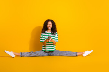 Wall Mural - Full size photo of pretty young girl split legs use phone wear striped t-shirt isolated on yellow color background