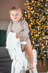 Family. A beautiful little blond boy of 1 year old on a wooden horse on the background of a Christmas tree. The concept of celebrating Christmas and New Year.