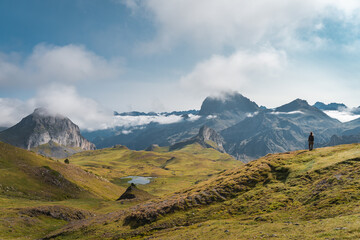 a lone hiker marvels at rugged mountains under a clear sky with scattered clouds on an alpine expedi