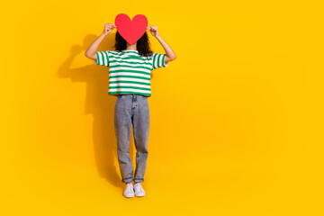 Wall Mural - Full size photo of pretty young girl cover face heart empty space wear striped t-shirt isolated on yellow color background