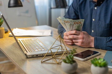 Close-up hands of businessman counting cash money dollar checking salary enjoy richness at workplace with laptop. Happy freelancer guy calculating currency profit financial savings at home office desk