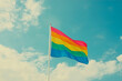© Ivan Traimak - Colorful rainbow flag waving proudly against a bright blue sky with white clouds during a sunny day at a public celebration. Generative AI