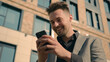 © Yuliia - Happy successful caucasian man businessman male guy online winner checking email reading good news using smartphone in city outdoors near office centre enjoying success celebrating victory on phone