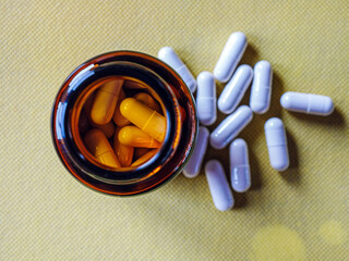 Top view of pills capsules in pill bottle on yellow background. White pills capsules medicine or  vitamin capsules