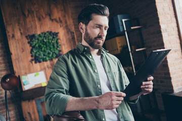 Photo of attractive young man read contract report wear green shirt comfortable modern office loft room interior indoors workspace