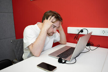 Poster - An IT specialist programmer is visibly stressed while working on a laptop in a coworking space. The bright red backdrop adds to the tension of the moment
